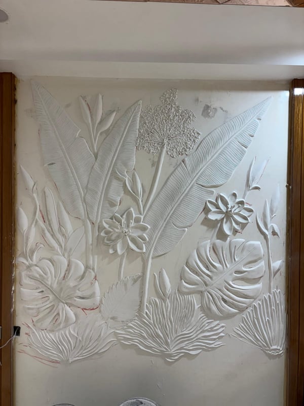 Hand-sculpted white plaster wall mural of tropical banana leaves, monstera and lotus blooms between wooden door frames, Hyderabad