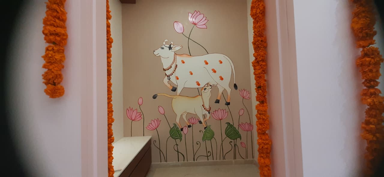 Pooja room with a hand-painted Pichwai-style cow and calf among lotus flowers, framed by marigold garlands, Hyderabad