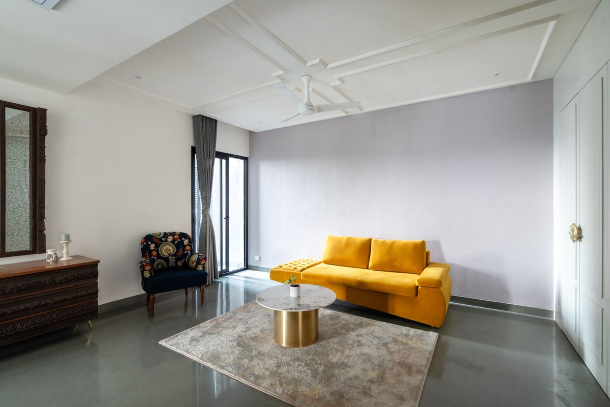 Drawing room with a mustard-yellow sofa, navy floral chair, round marble-top table and polished concrete floor, Hyderabad