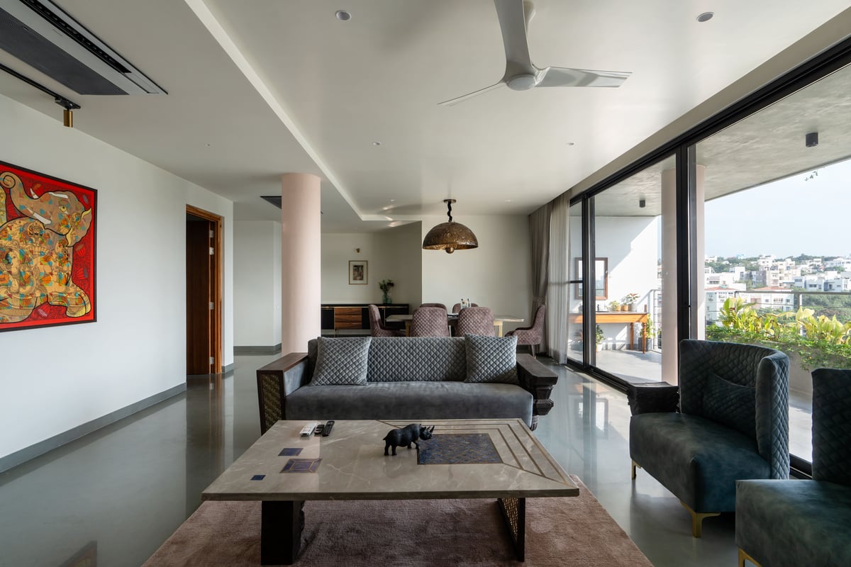Open living room with grey quilted sofas, marble coffee table, bold abstract painting and balcony city views, Hyderabad