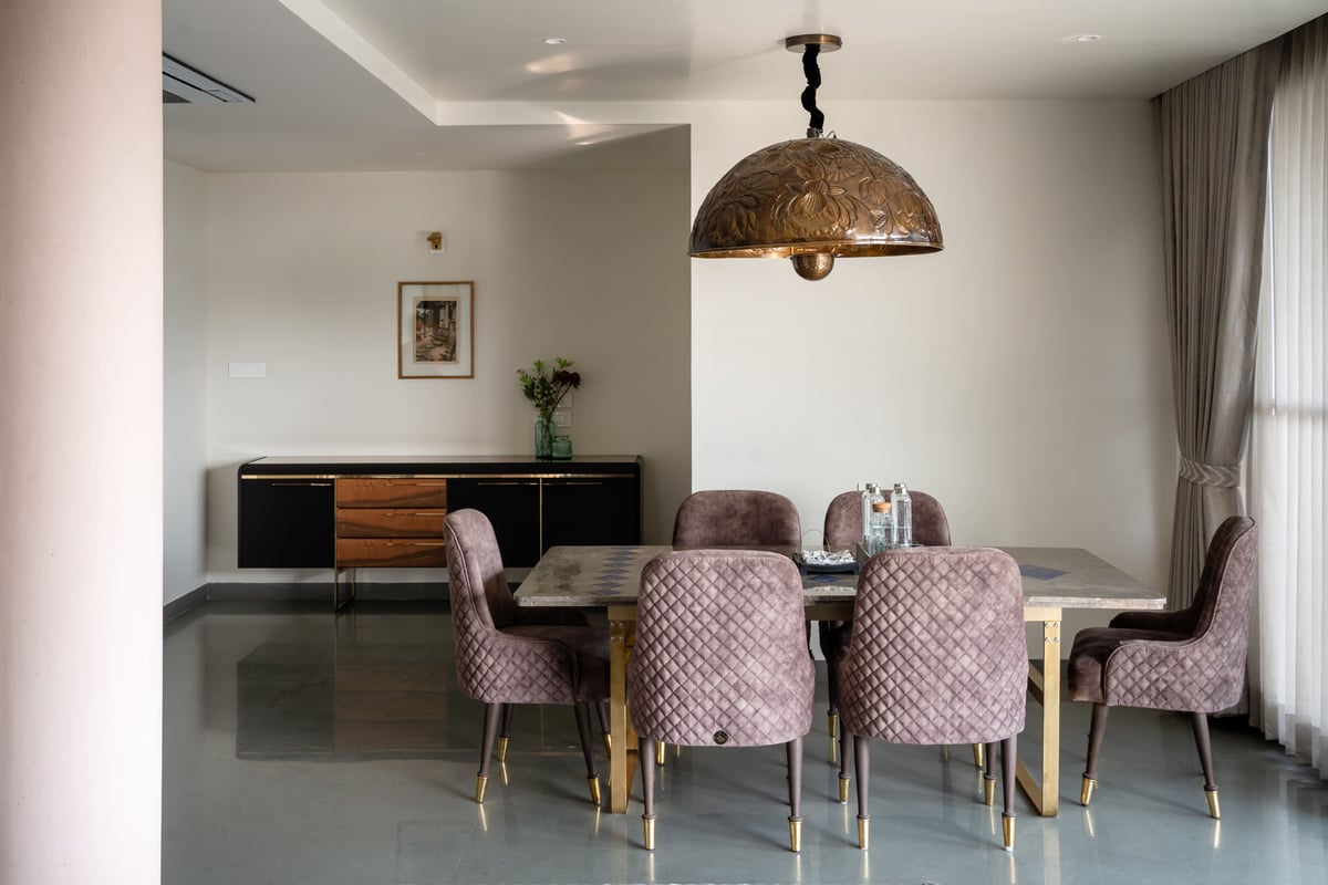 Dining area with marble-top table, mauve velvet tufted chairs and an ornate carved dome pendant light, Hyderabad