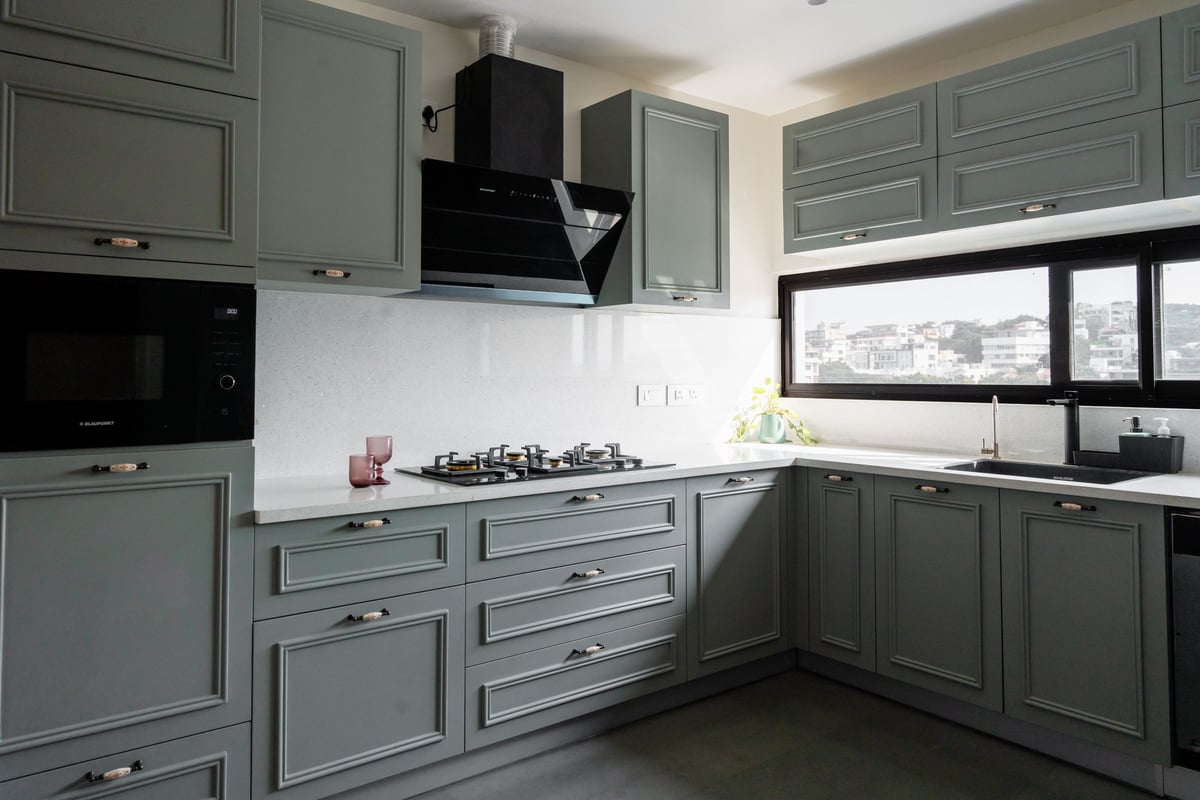 Sage-green shaker kitchen in Hyderabad with black chimney, white quartz counters, gas hob and a city-view window