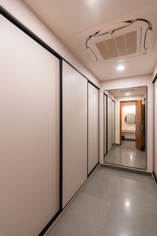 Walk-in wardrobe lobby with floor-to-ceiling white shutters and tall framed mirror reflecting the ensuite, Hyderabad
