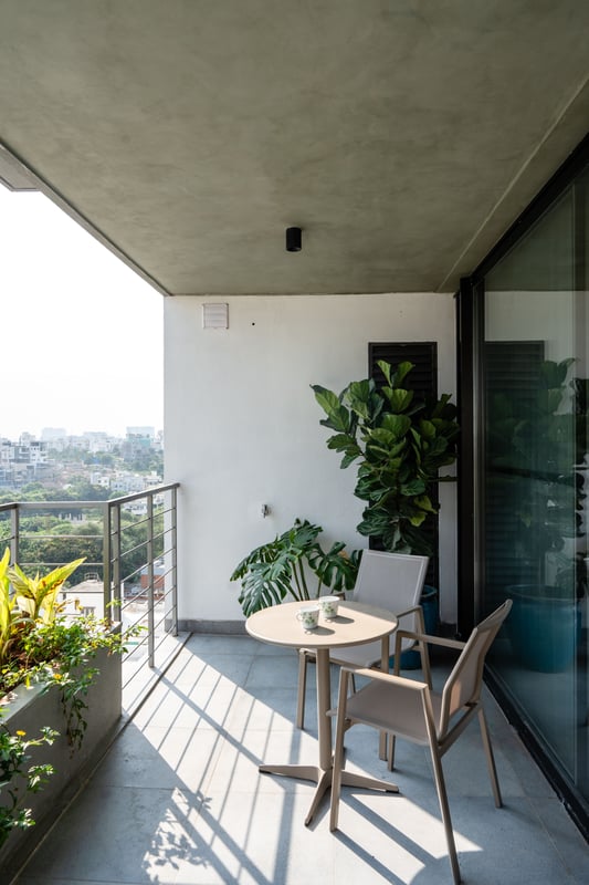 Balcony with bistro table and chairs, fiddle-leaf fig planters and city skyline view under a concrete soffit, Hyderabad