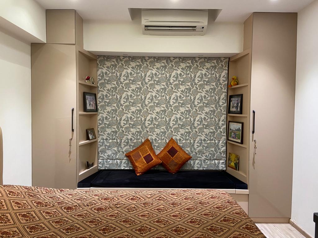 Master bedroom in Hyderabad with botanical-print niche, padded bench, framed photos and patterned bedspread