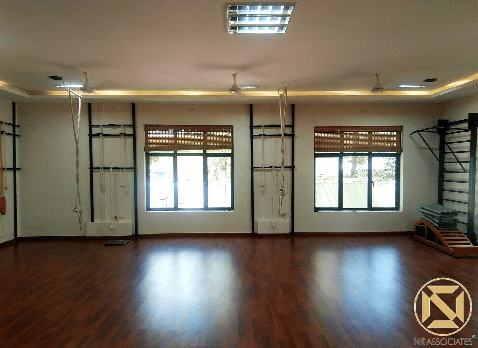 Yoga therapy hall with polished timber floor, wall-mounted rope props, bamboo window blinds and ceiling fans, Hyderabad