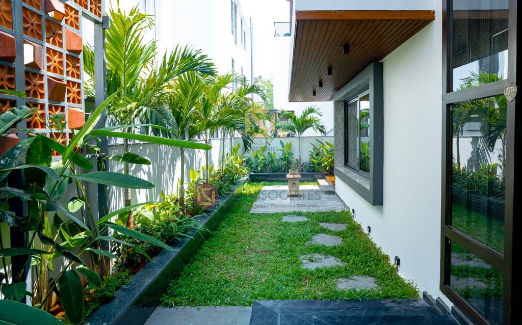 Landscaped side garden with stepping-stone lawn path, layered tropical planters and a terracotta jaali screen, Hyderabad residence