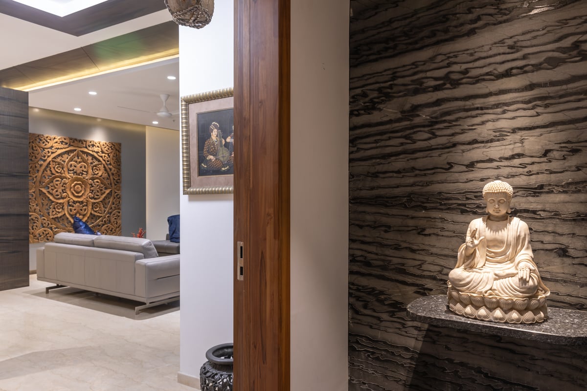 Home foyer with dark textured stone wall, carved Buddha idol on a floating shelf and mandala wood panel beyond, Hyderabad