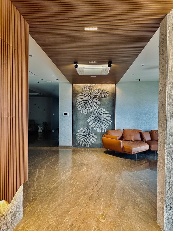 Foyer with wood-slat ceiling, metallic monstera-leaf wall art, tan leather sofa and polished beige marble flooring, Hyderabad