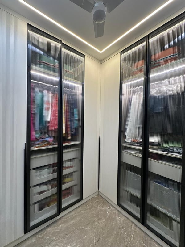 Walk-in wardrobe with black-framed fluted glass doors, LED cove lighting and pull-out drawers, Hyderabad