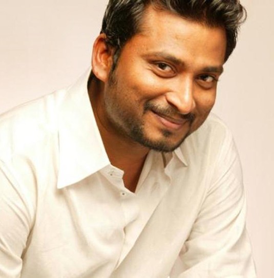 Portrait of a smiling man in a white collared shirt against a soft beige backdrop