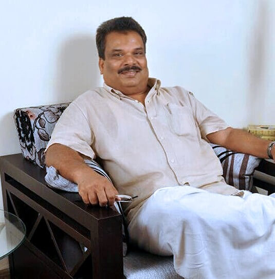 Portrait of a smiling man seated in a dark-wood-armed lounge chair against a plain white wall