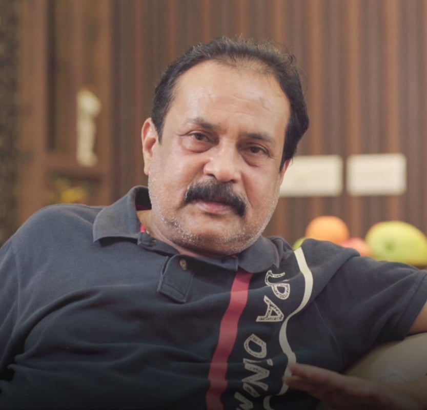 Portrait of a smiling man seated on a sofa in a warm wood-panelled living room, Hyderabad home